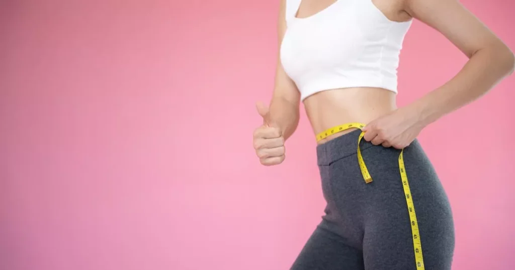 A slender girl in sportswear measures her body and waist with a meter