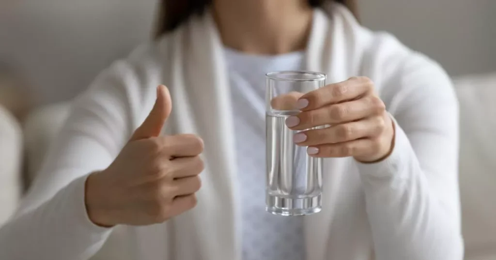 Women giving thumbs up holding glass of water